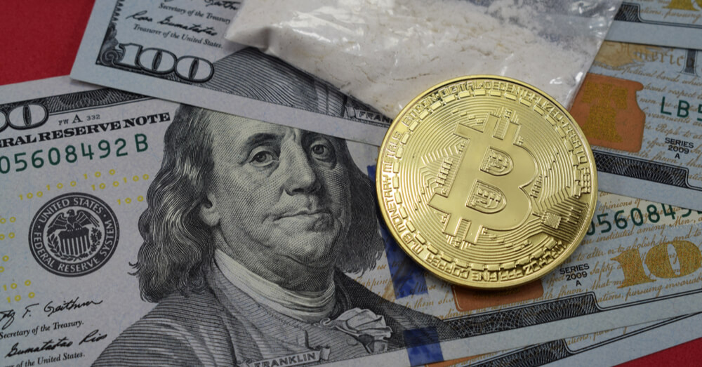 Uma imagem de dólares americanos, drogas e um Bitcoin em uma superfície vermelha