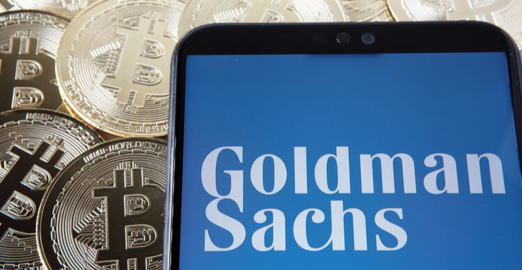 Imagem do logotipo do Goldman Sachs num smartphone em cima de Bitcoins